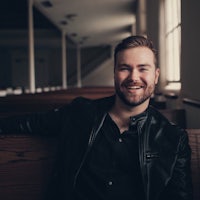 a man in a black jacket sitting on a bench in a church